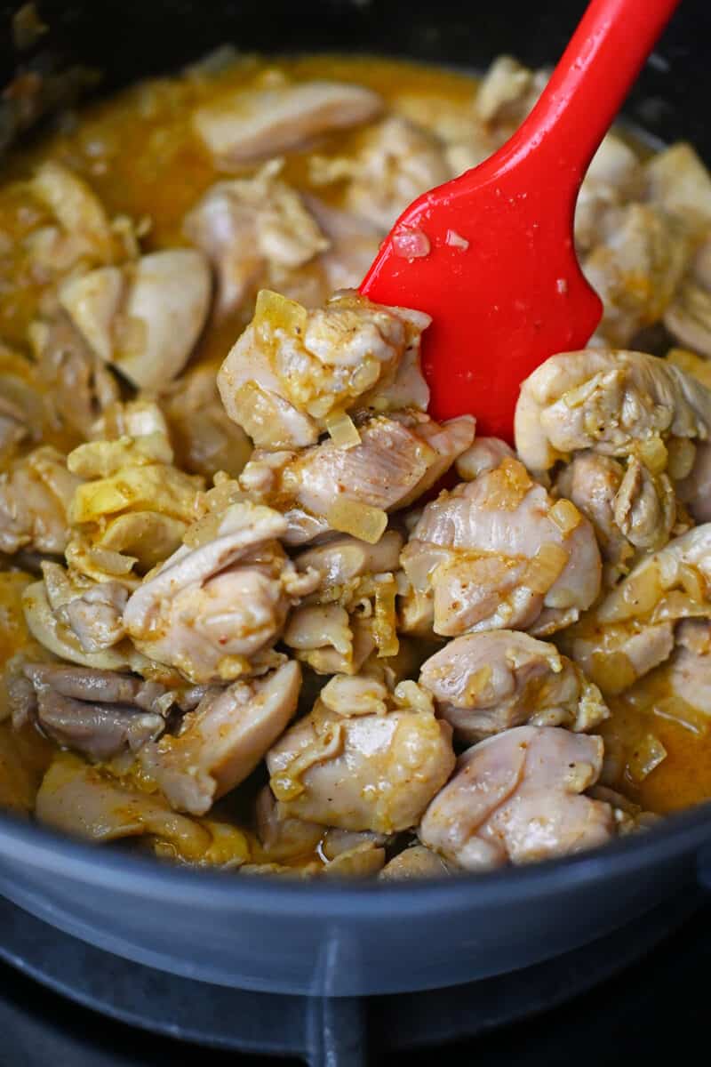 A closeup photo of cut-up cooked chicken thighs and spices in a pot.