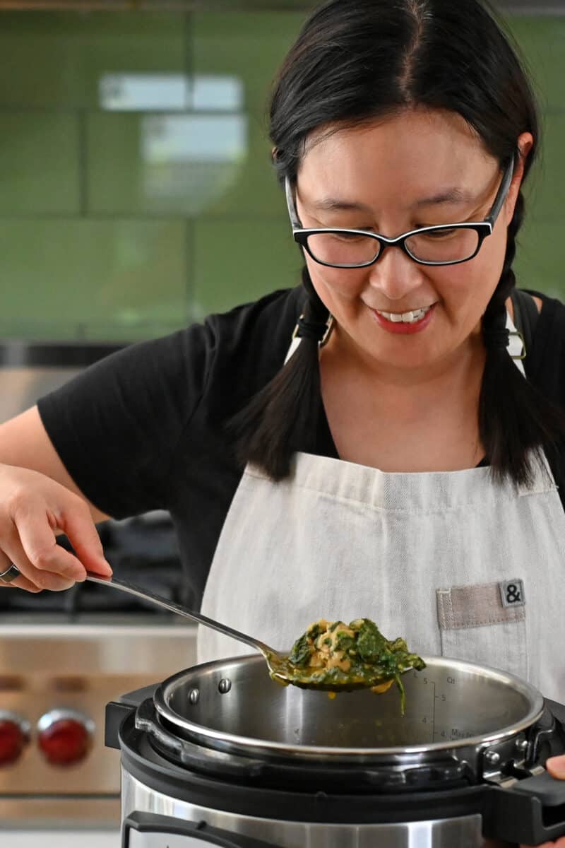 An Asian woman is scooping up some chicken and spinach curry from an Instant Pot.