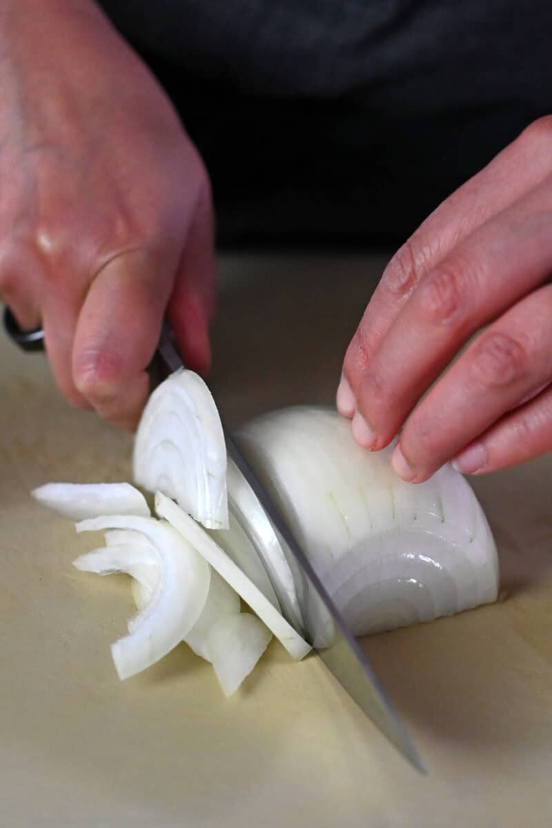 A closeup of a person thinly slicing half a raw onion for gyudon.