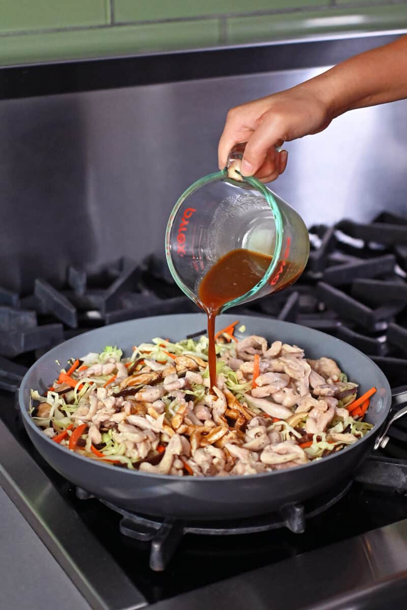 Pouring in the gluten free and paleo sauce to a skillet filled with Moo Shu Chicken.