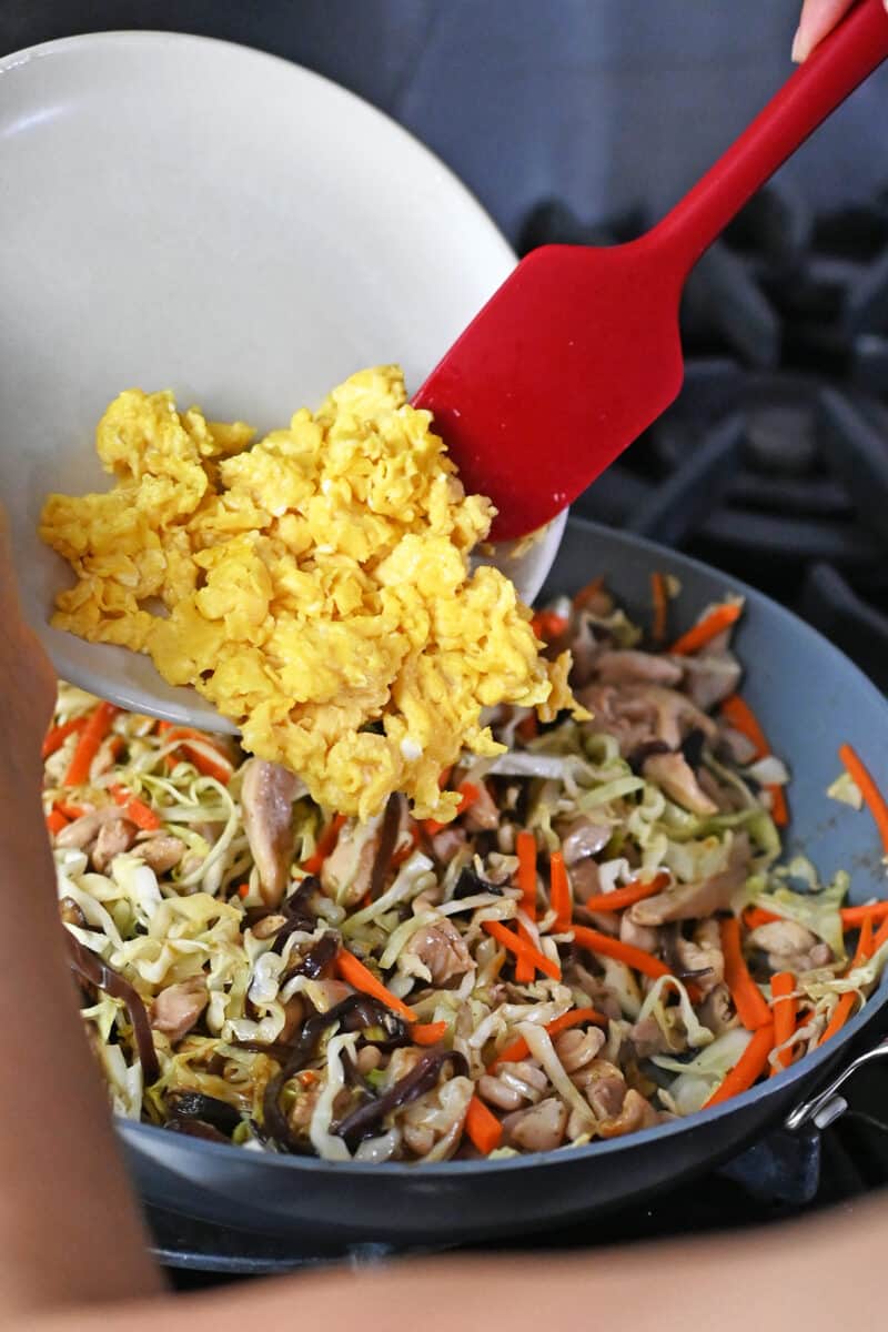 Adding a plate of cooked scrambled eggs into a skillet filled with Moo Shu Chicken.