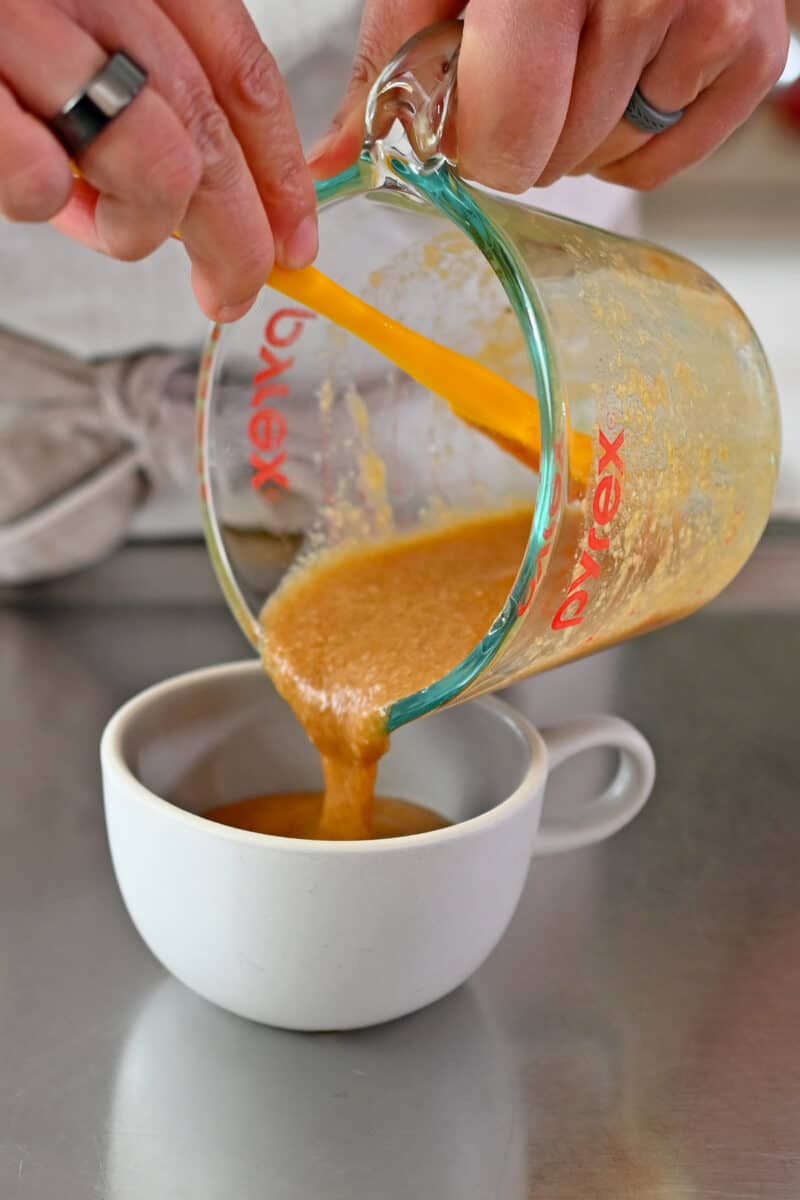 Pouring the gluten free mug cake batter into a small coffee cup.