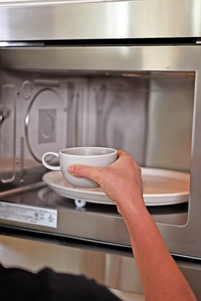 Placing a coffee mug filled with gluten free cake batter into a microwave with a turntable.