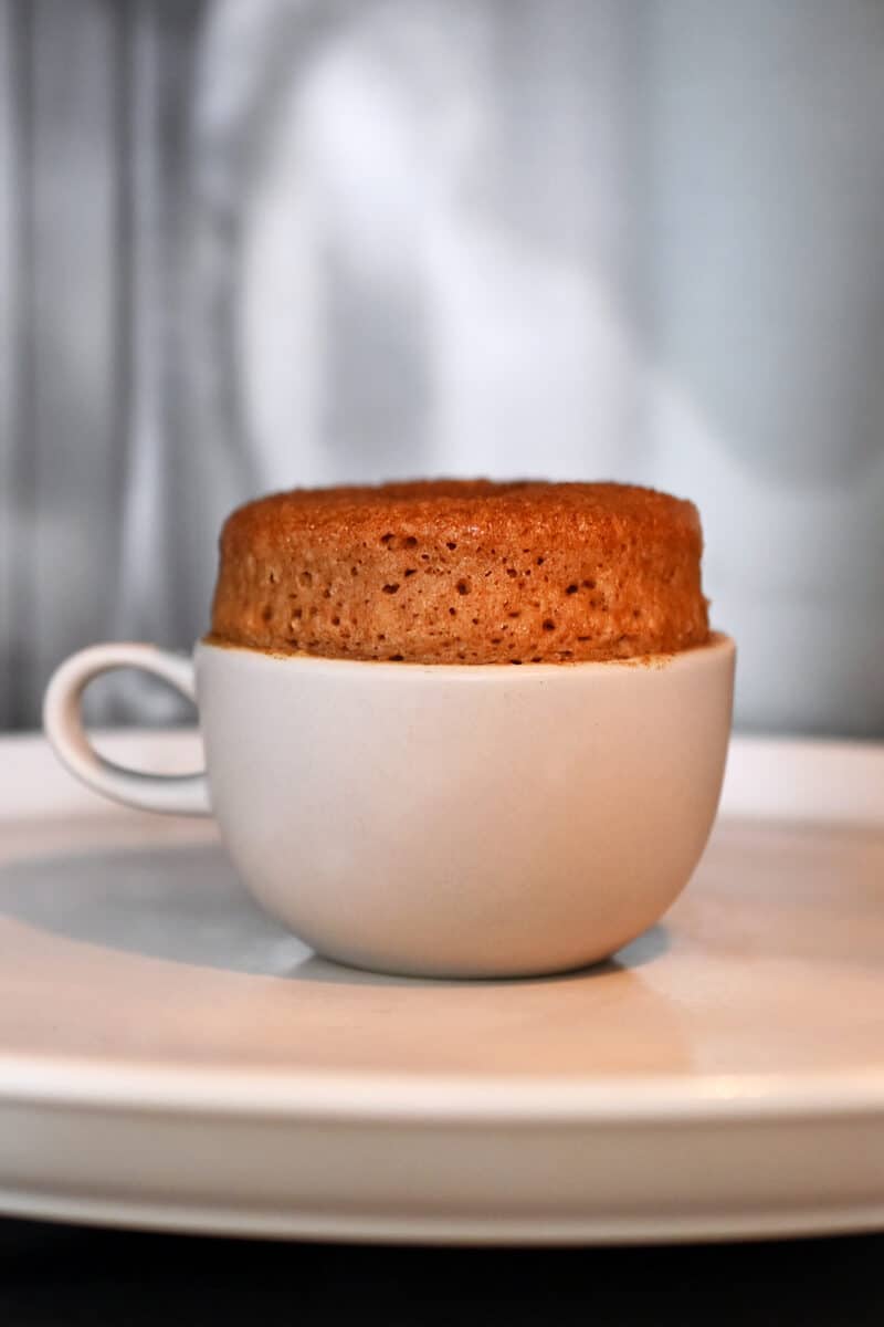 A fully cooked apple mug cake inside of a microwave where the cake is golden brown and about one inch above the rim.