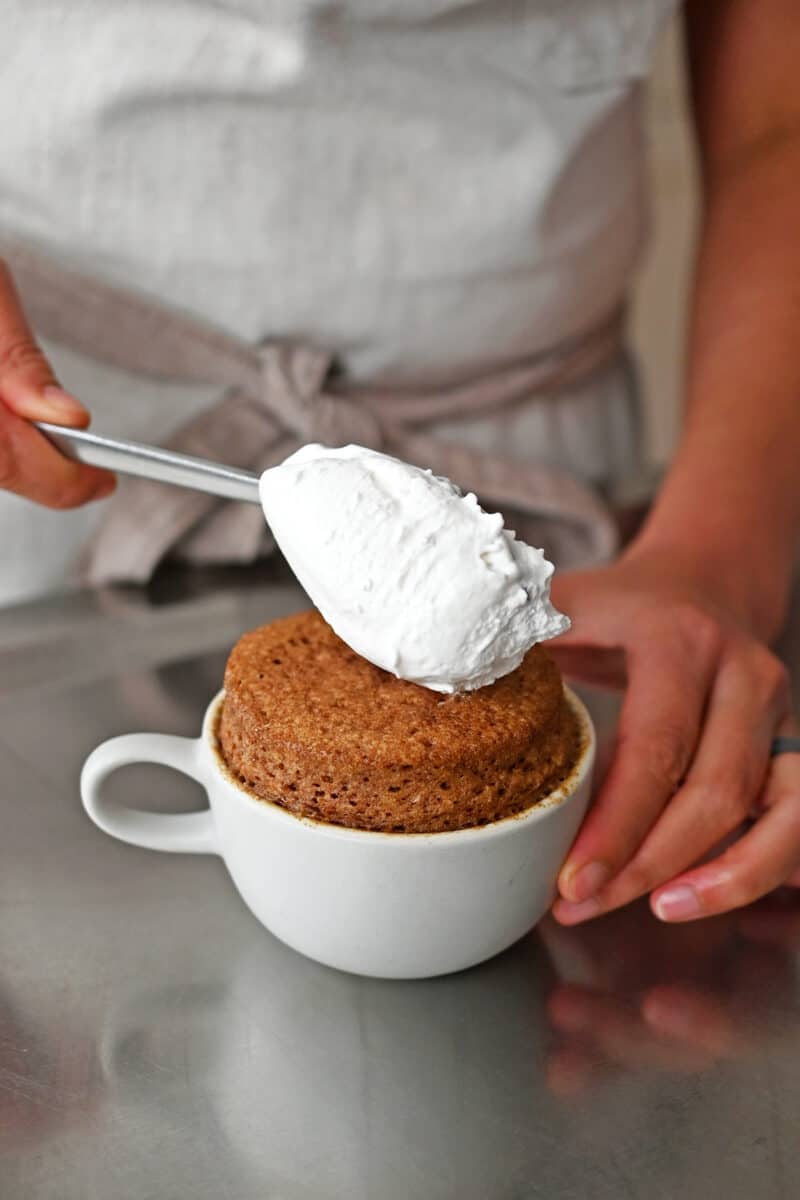 Adding a spoonful of whipped coconut cream on top of a gluten free mug cake.