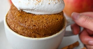 A gluten free and paleo apple mug cake topped with whipped coconut cream.