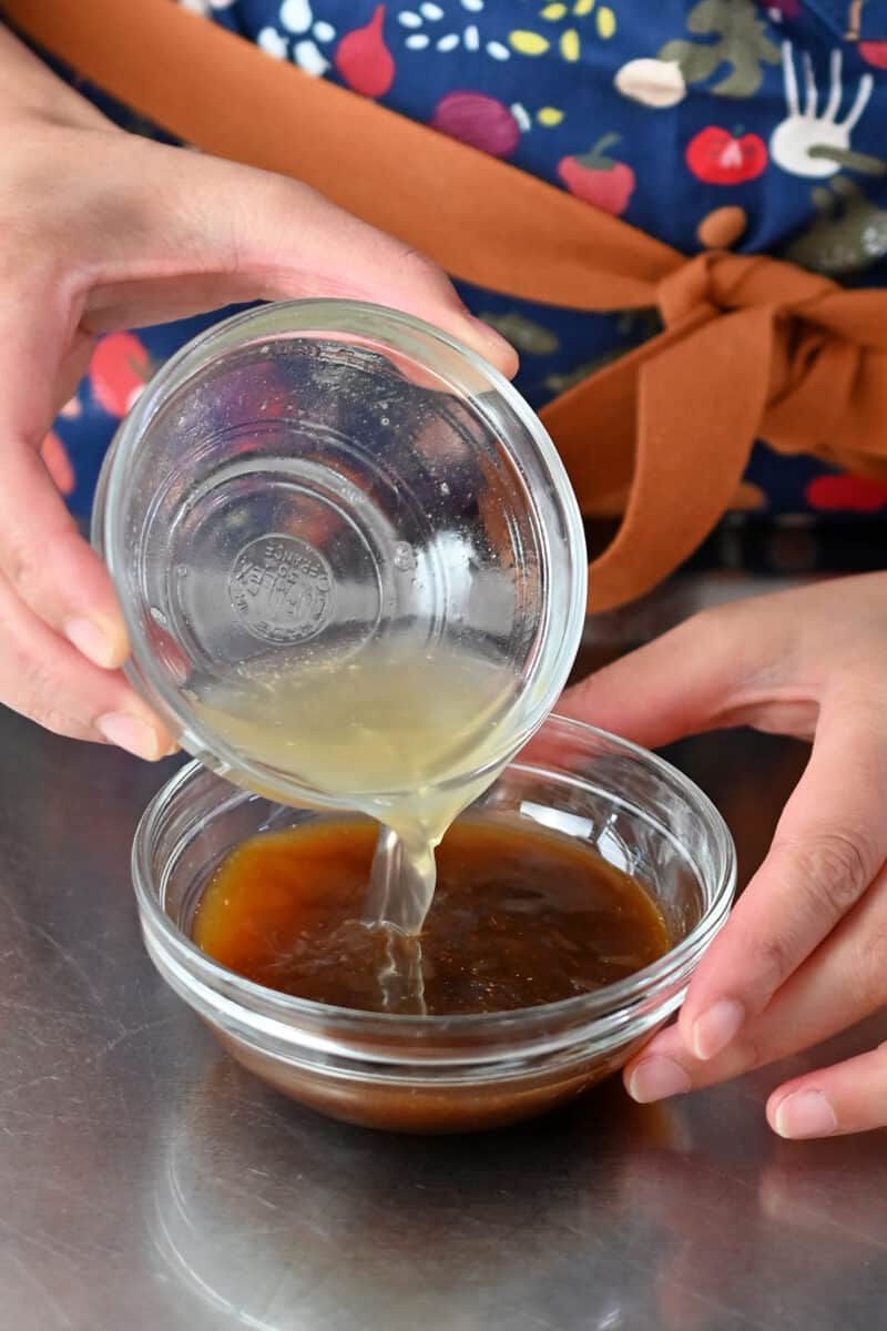Pouring some clear broth into a bow filled with a brown liquid, All-Purpose Stir-Fry Sauce.