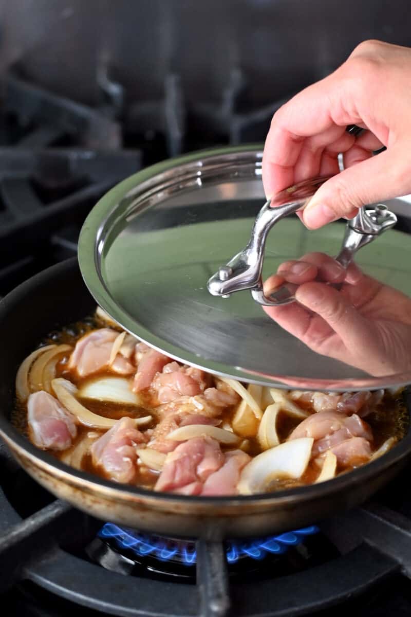 Placing a lid on a small skillet filled with chicken and onion in a simmering brown sauce.