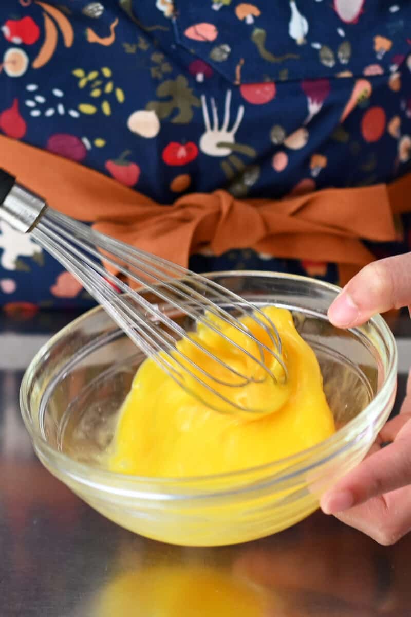 Whisking an egg in a clear glass bowl with a whisk.