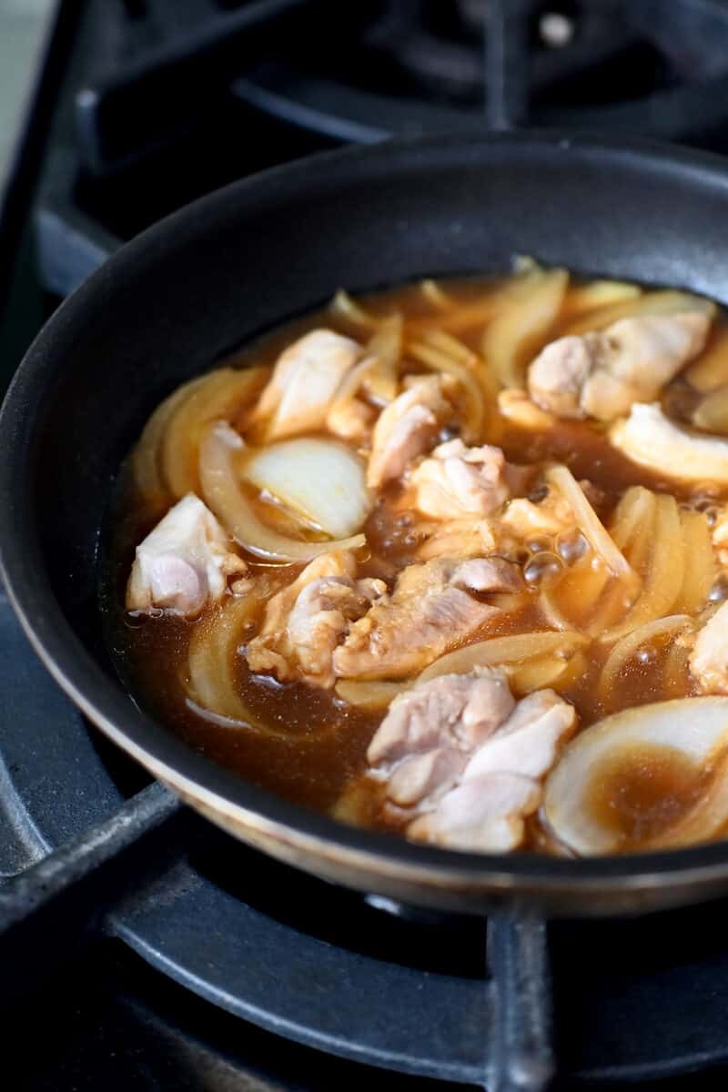 A skillet filled with cooked chicken pieces and sliced onion in a brown sauce.