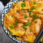 A blue and white bowl of paleo and gluten free oyakodon, a Japanese dish with simmered chicken and scrambled eggs.
