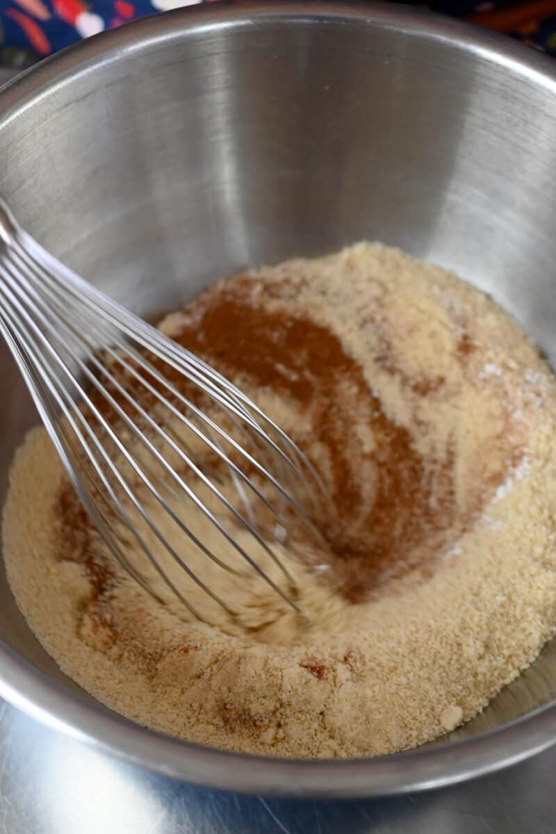 A closeup of the dry ingredients for paleo pumpkin bars being whisked in a large metal mixing bowl.