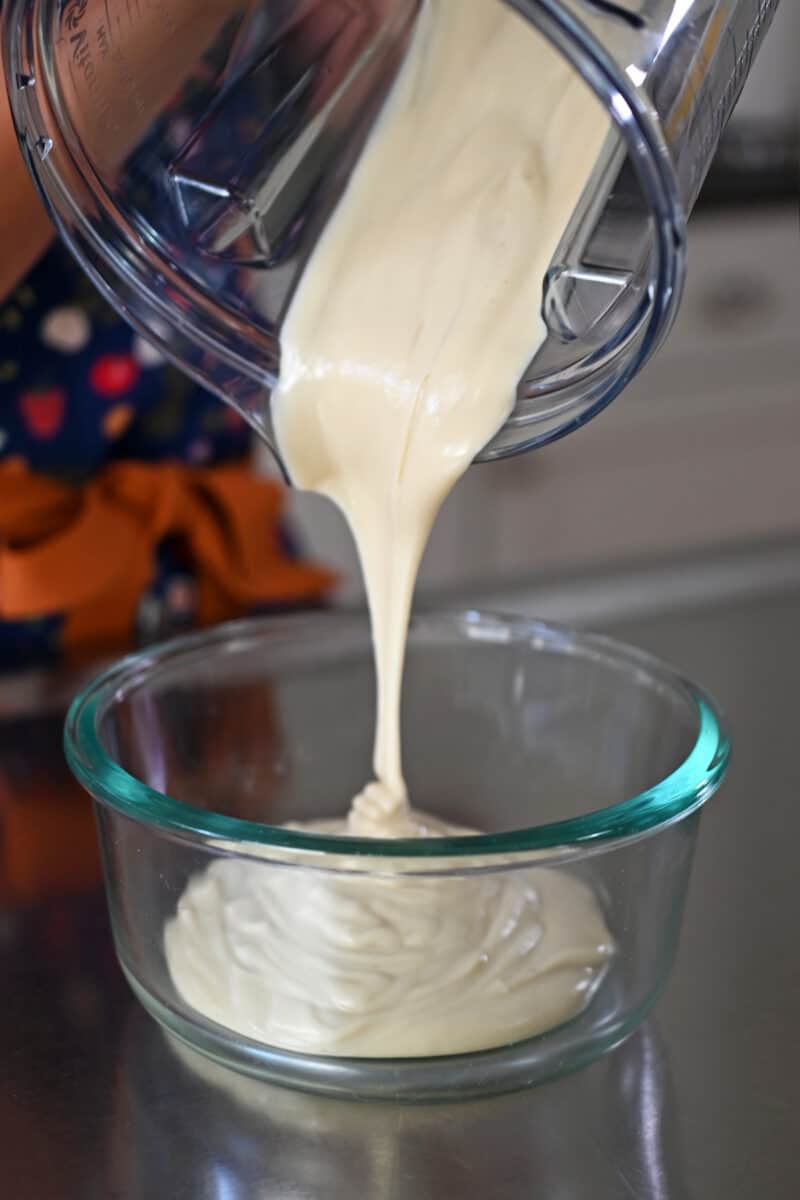 Pouring vegan cream cheese frosting from a blender into a glass storage container.