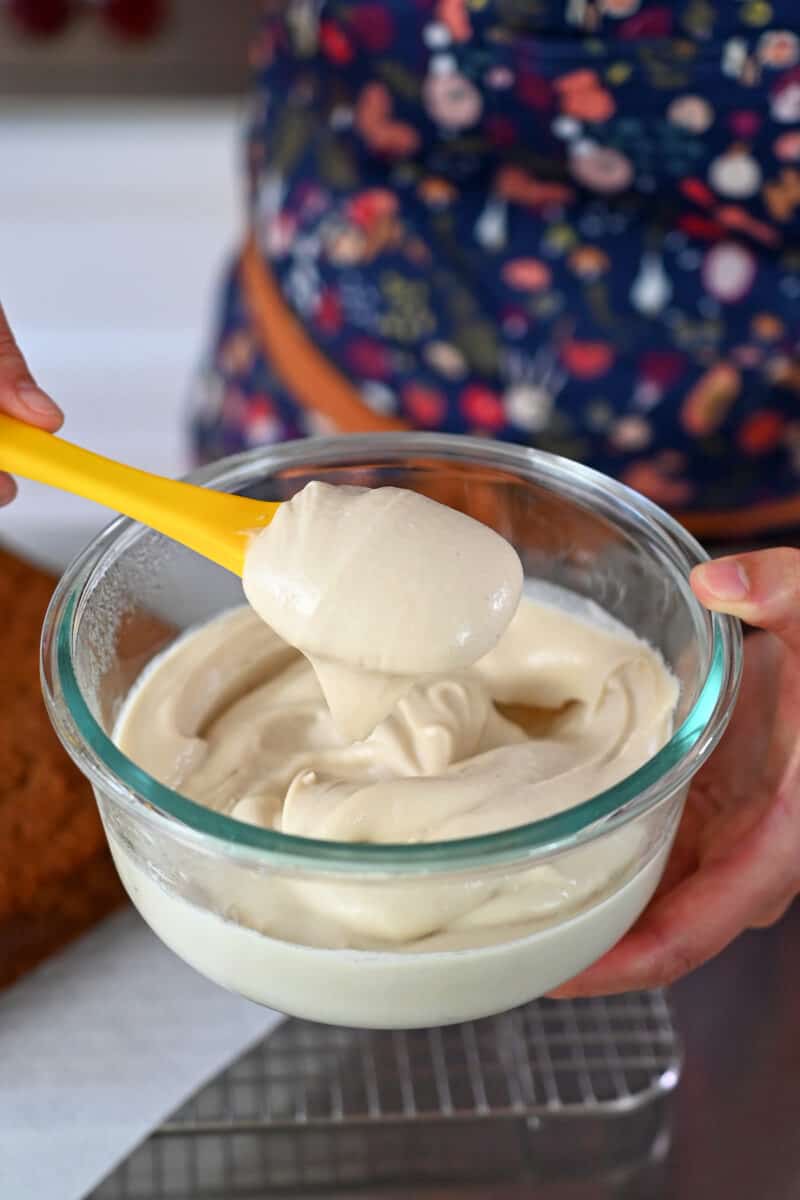 A spatula dipped in dairy-free paleo and vegan cream cheese frosting in a glass bowl.