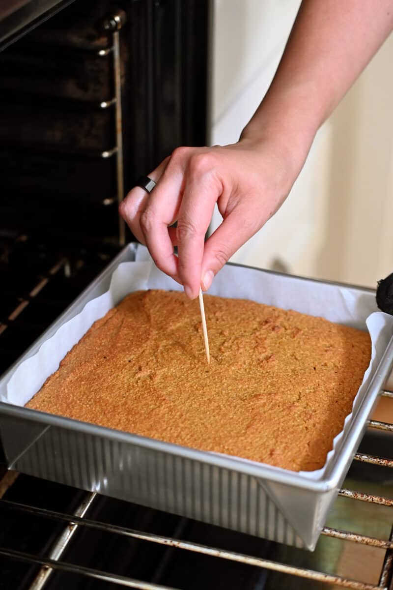 A toothpick is being inserted into a pan filled with baked pumpkin bars. 
