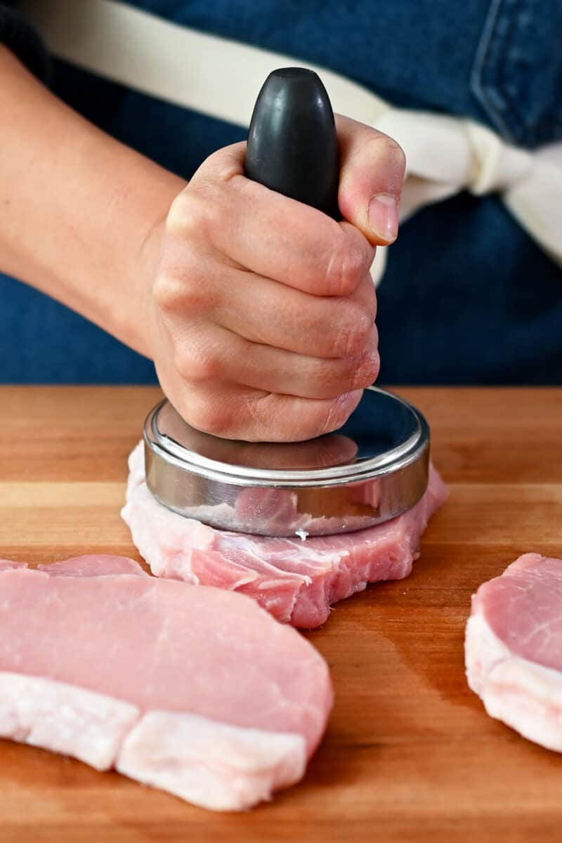 A meat pounder is smashing down on a boneless pork chop.