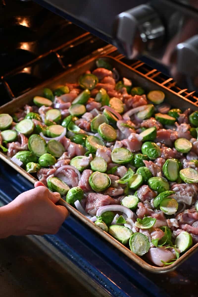 Placing a sheet pan with chicken and Brussels sprouts into the oven.