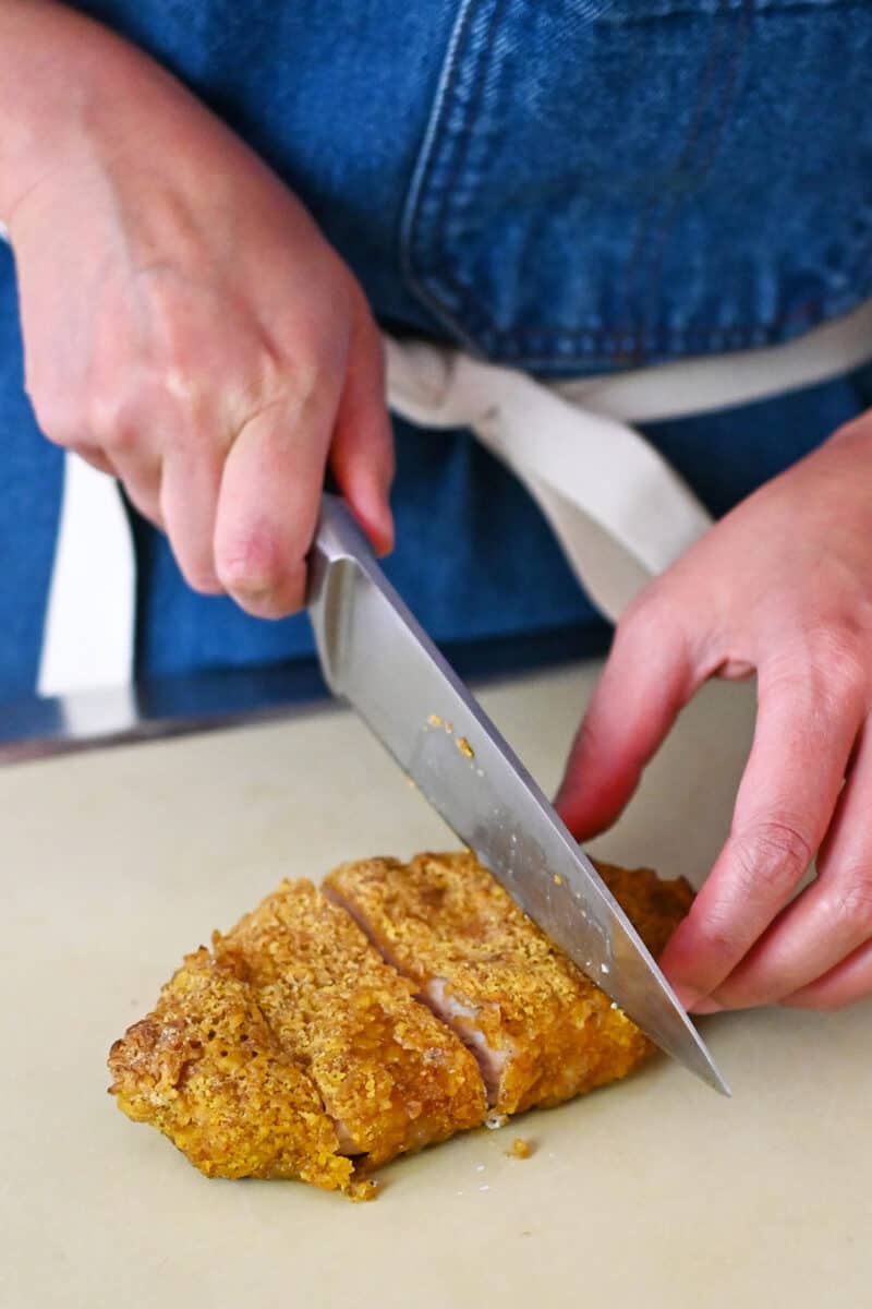 Someone in a blue apron is slicing up a homemade tonkatsu.