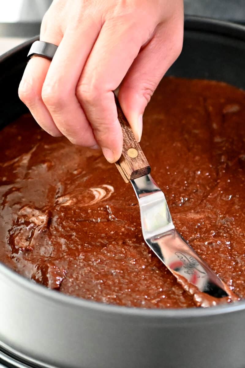 A hand is using an offset spatula to smooth the top of Torta Caprese cake ready for the oven.