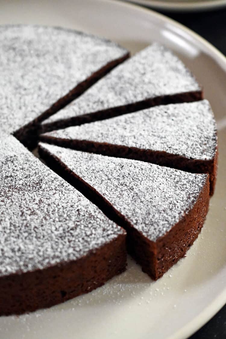 A close up shot of a Torta Caprese, a classic Italian almond flour chocolate cake with three slices cut into it.