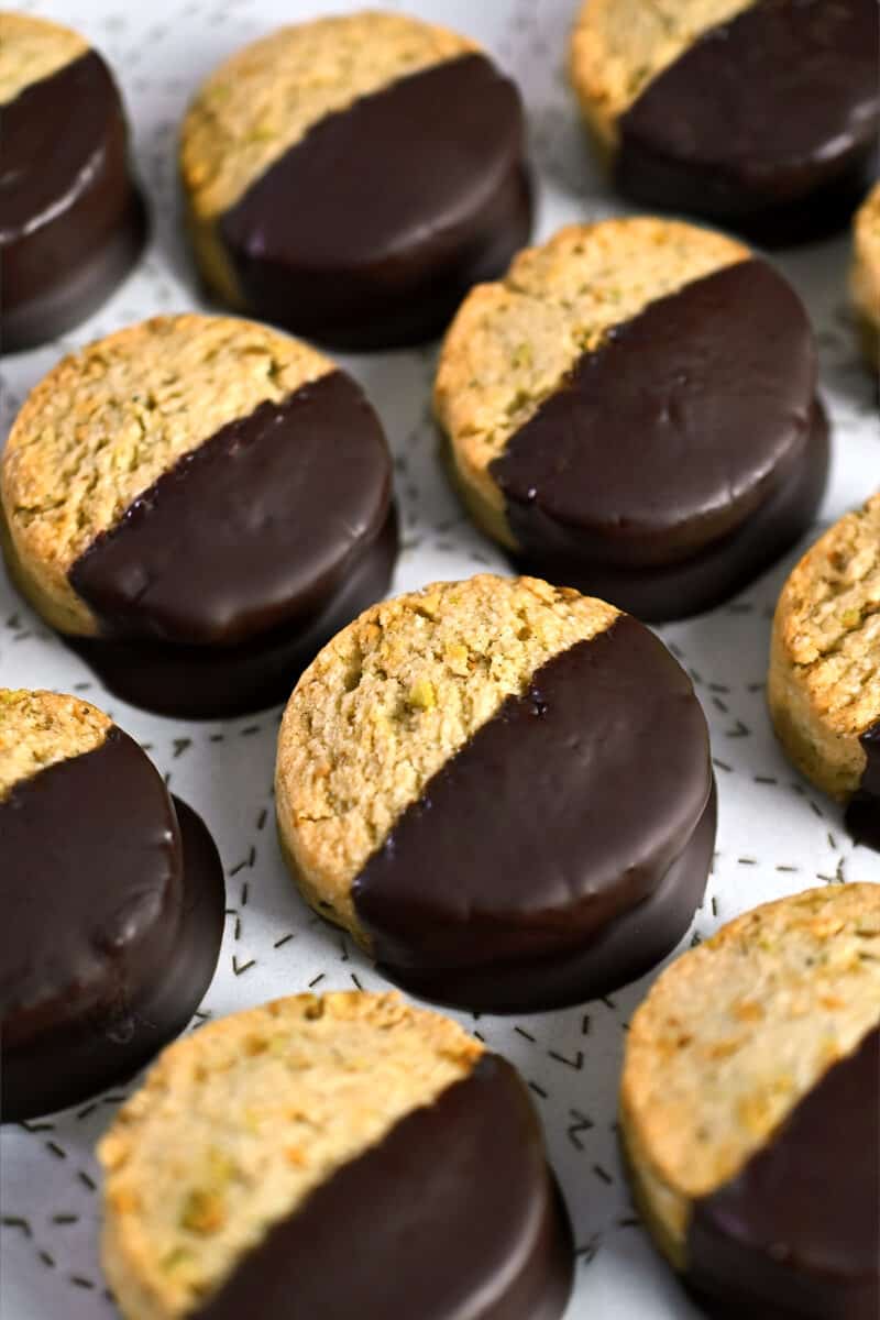 A closeup of a plate of chocolate dipped pistachio cookies.
