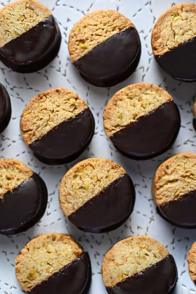 A closeup of chocolate dipped pistachio cookies on a white plate.