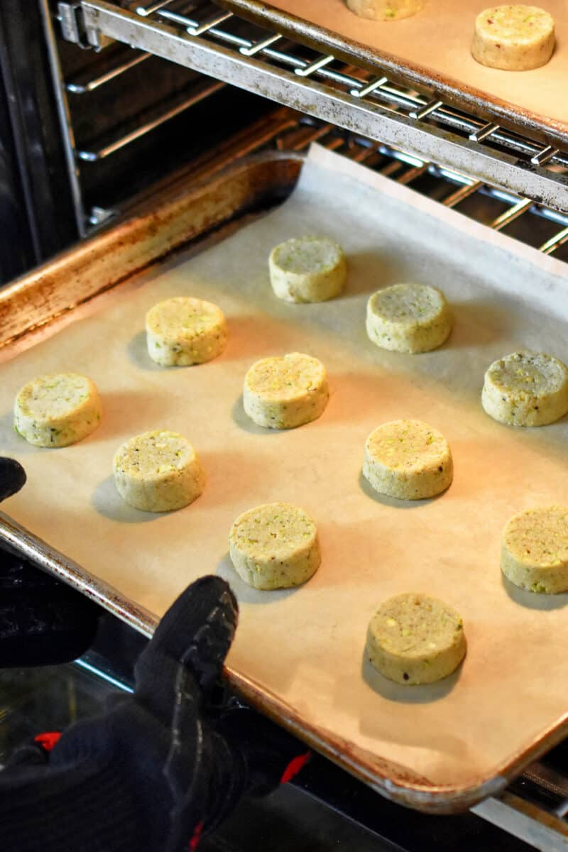 Placing a second tray of pistachio cookies into an open oven.