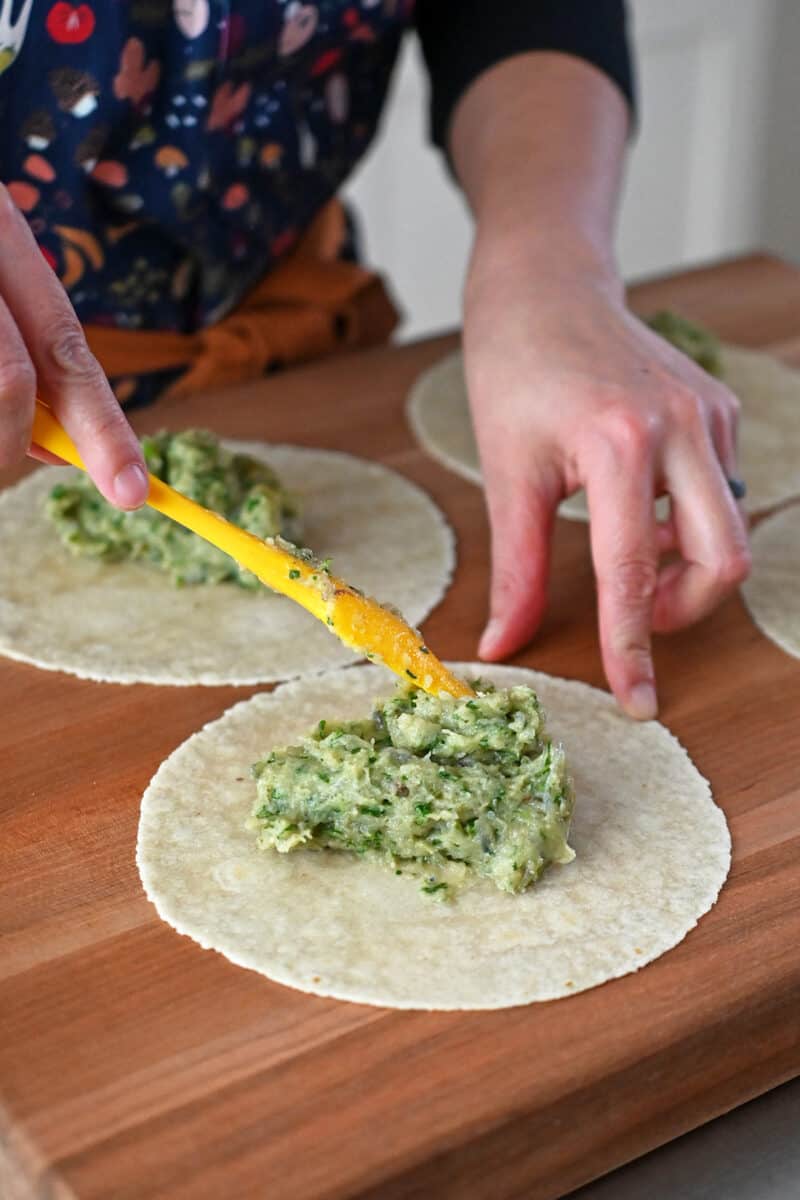 A spatula is spreading one fourth of the uncooked shrimp paste on a grain-free tortilla.
