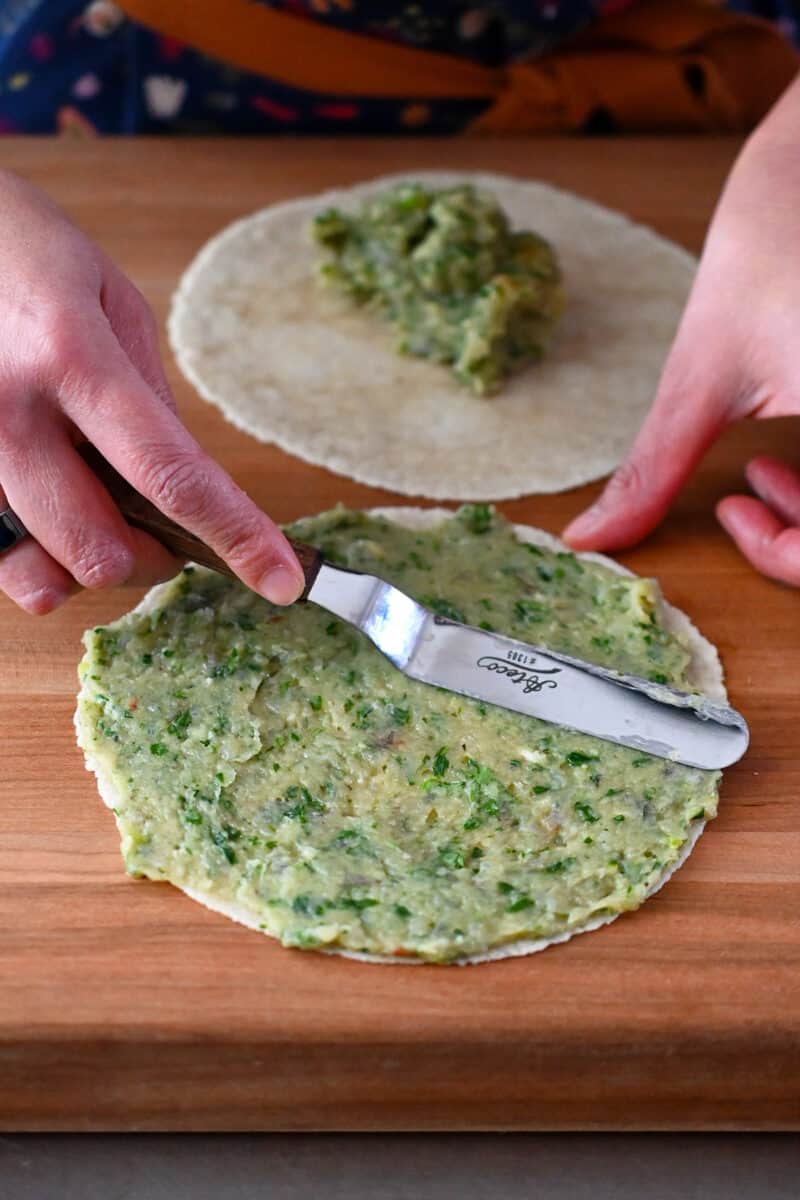 An offset metal spatula spreads the raw shrimp paste in a thin layer over a paleo almond flour tortilla.