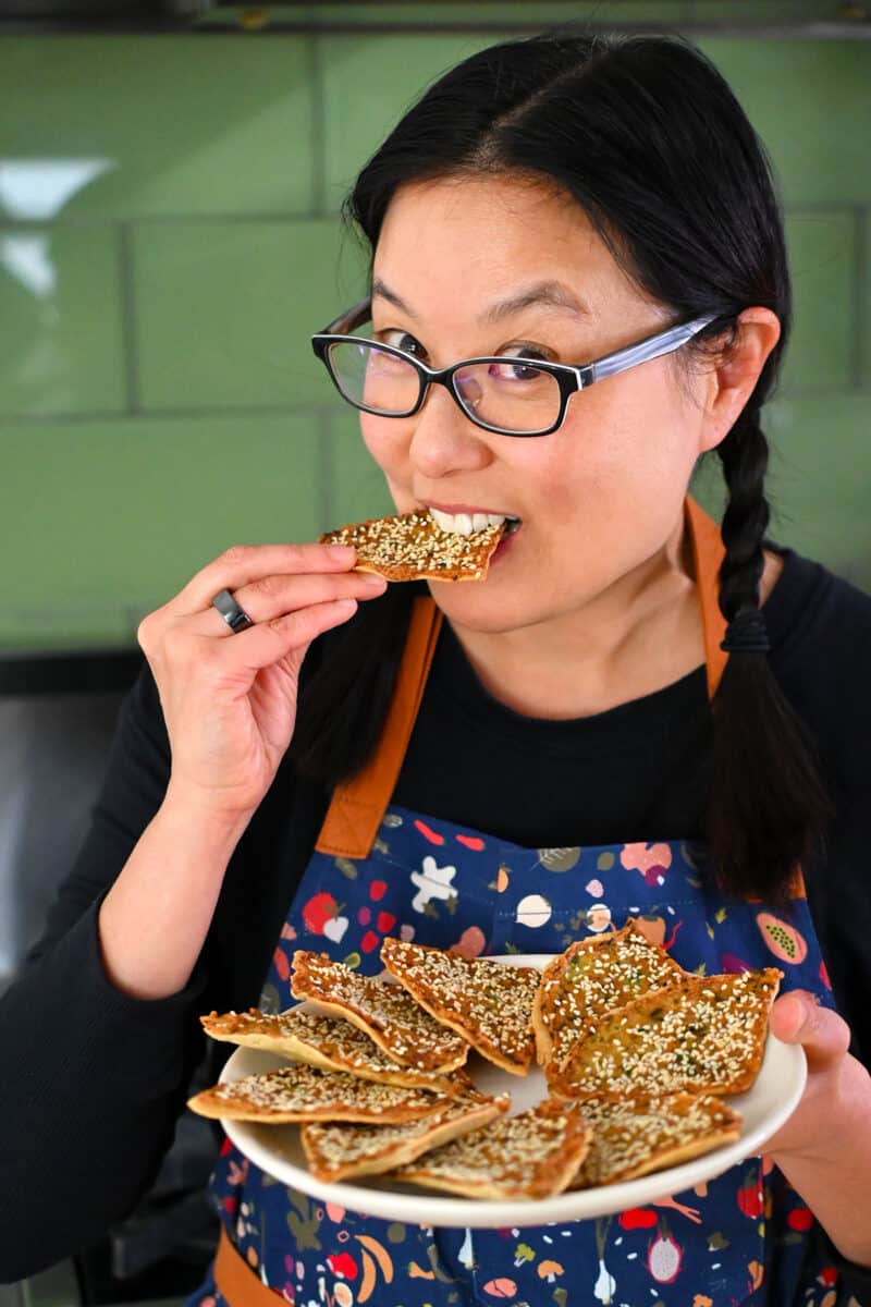 A smiling Asian woman is biting into a paleo shrimp toast.