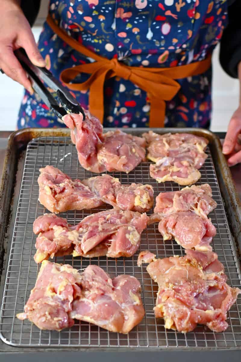 Placing boneless skinless chicken thighs on a wire rack in a rimmed baking sheet.