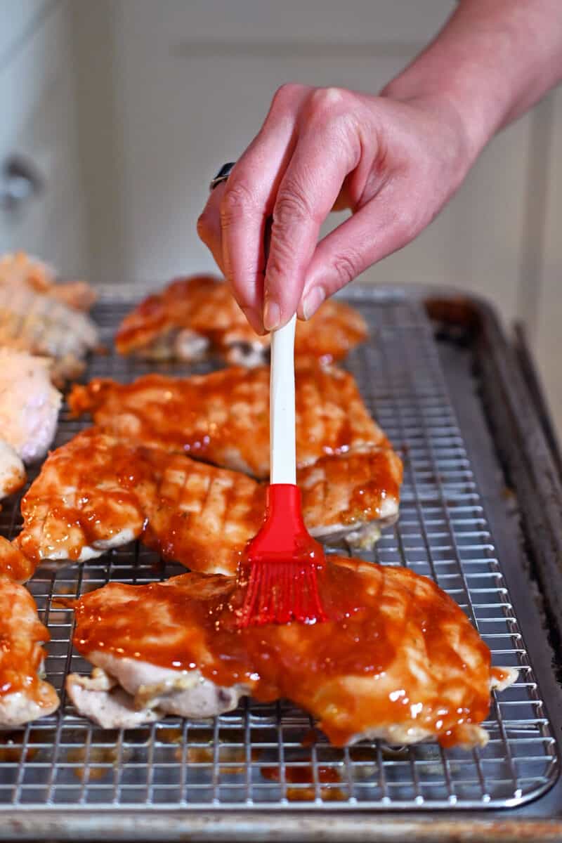 Brushing sauce on the top of boneless skinless chicken thighs that are mostly cooked.