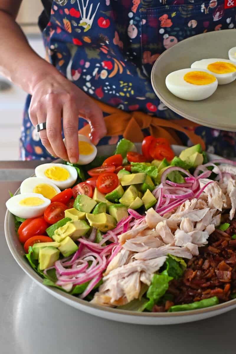 Placing halved hard boiled eggs on a Cobb salad.