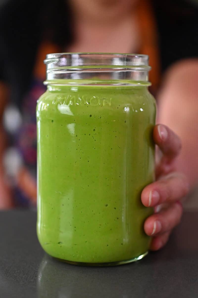 A hand is holding a mason jar filled with paleo, vegan, and Whole30 Green Goddess Dressing.