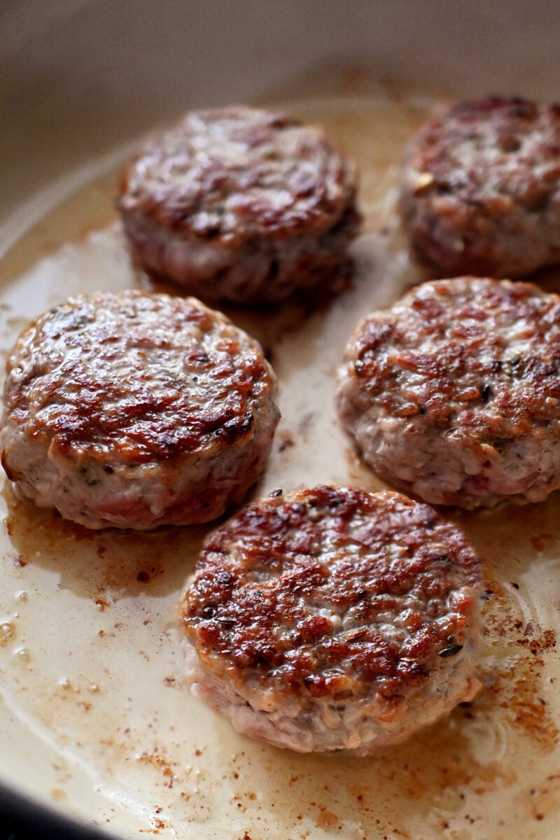 An enamel cast iron skillet filled with golden brown sausage patties.
