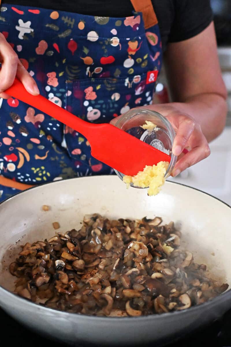 Adding minced garlic to a pan filled with sautéed mushrooms and onions.