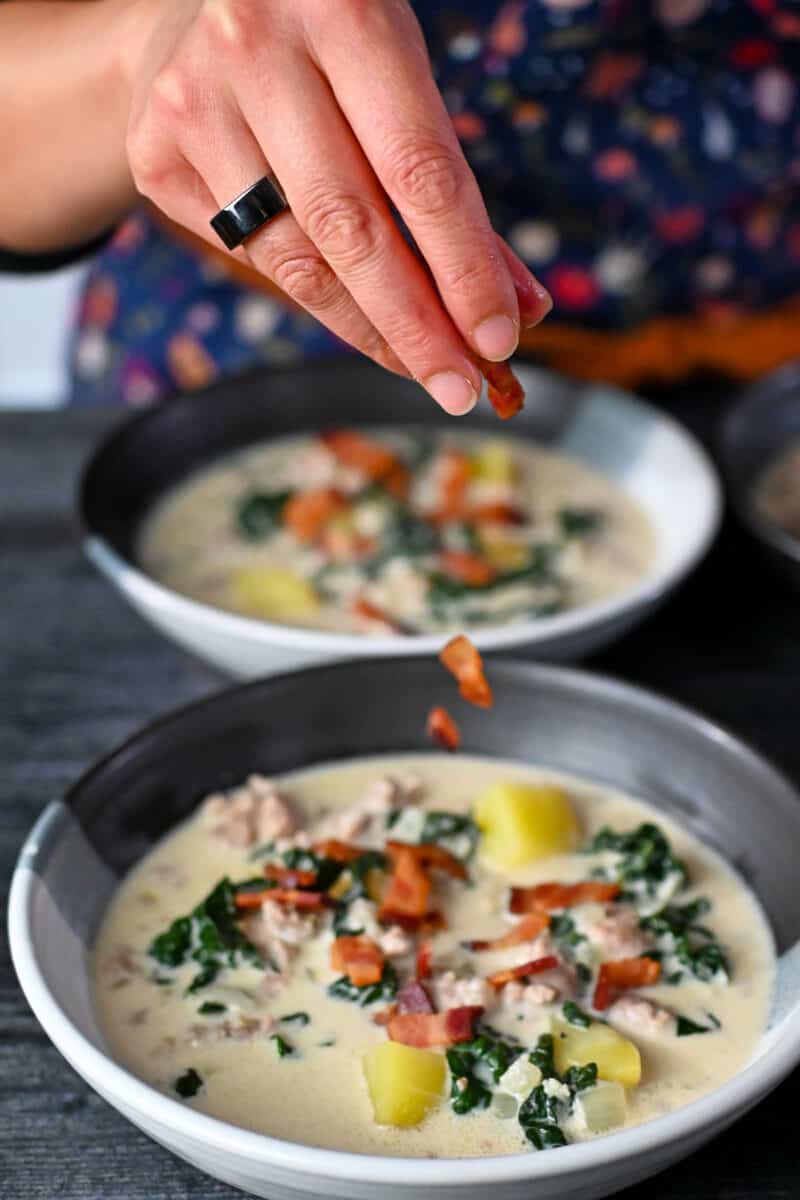 Adding crispy bacon bits to the top of bowls filled with Whole30 Zuppa Toscana.
