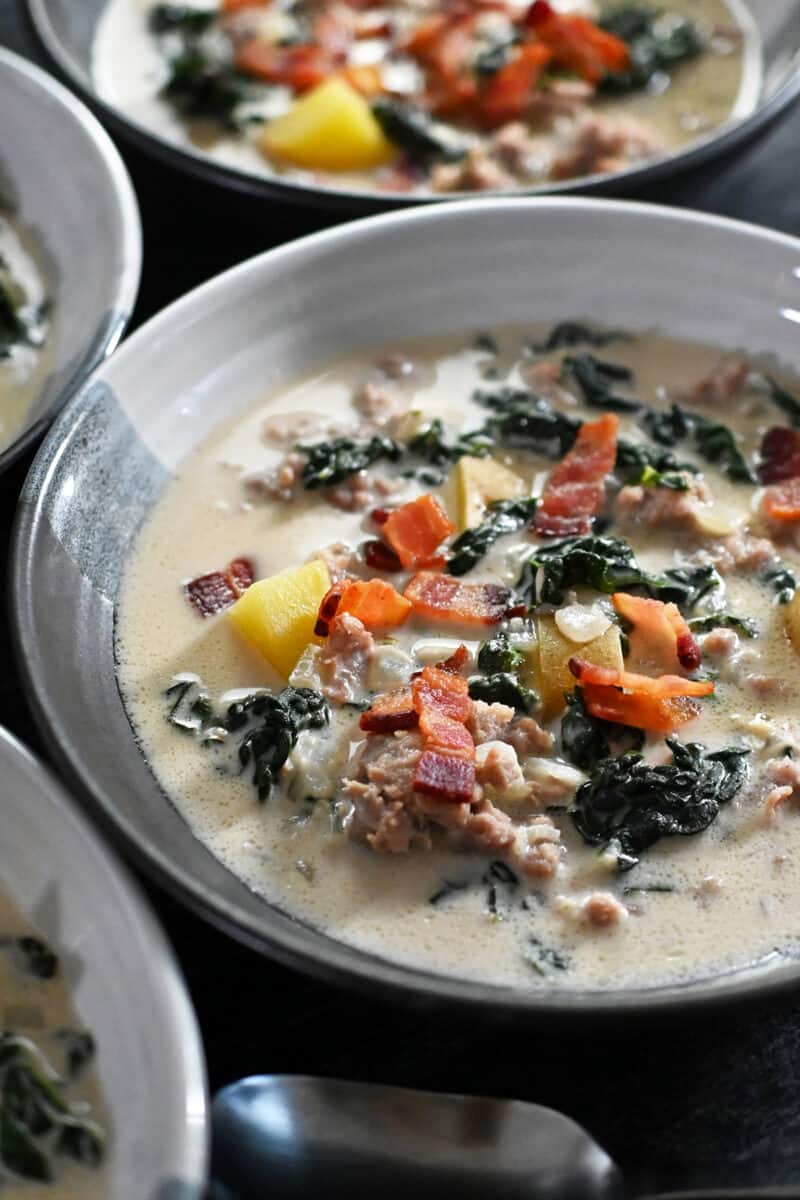A closeup of a bowl of Whole30 Zuppa Toscana soup topped with crispy bacon bits.
