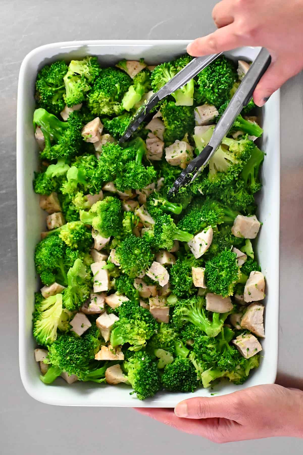 An overhead shot of a white casserole dish filled with seasoned cooked broccoli and cubed chicken.