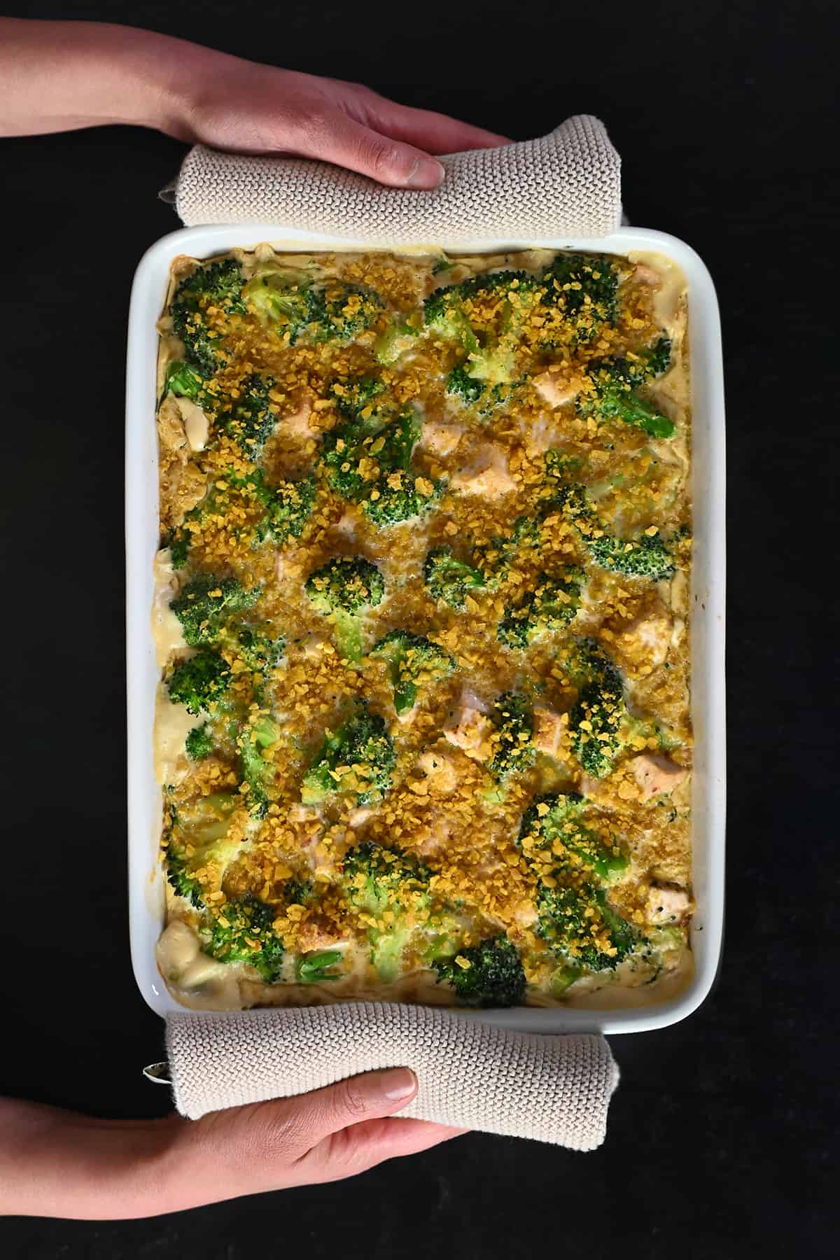 Two hands are holding a paleo chicken divan casserole right out of the oven.