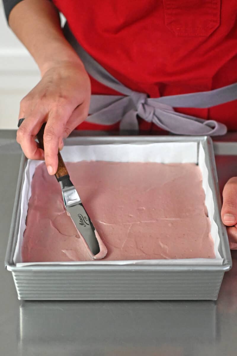 Using an offset spatula to smooth the top of the strawberry cheesecake bars.