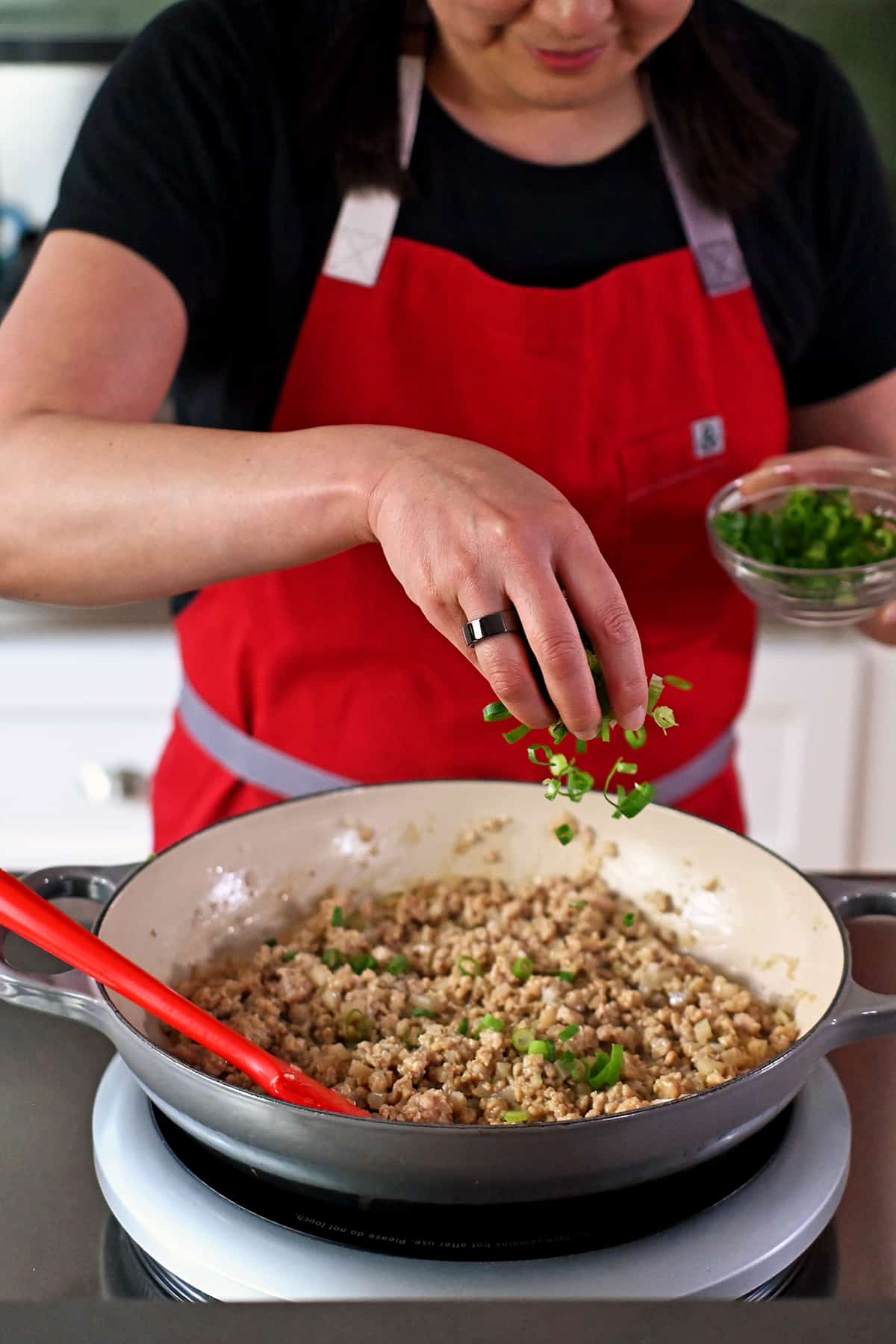 Sprinkling sliced green onions into a skillet filled with ground chicken lettuce wrap filling.