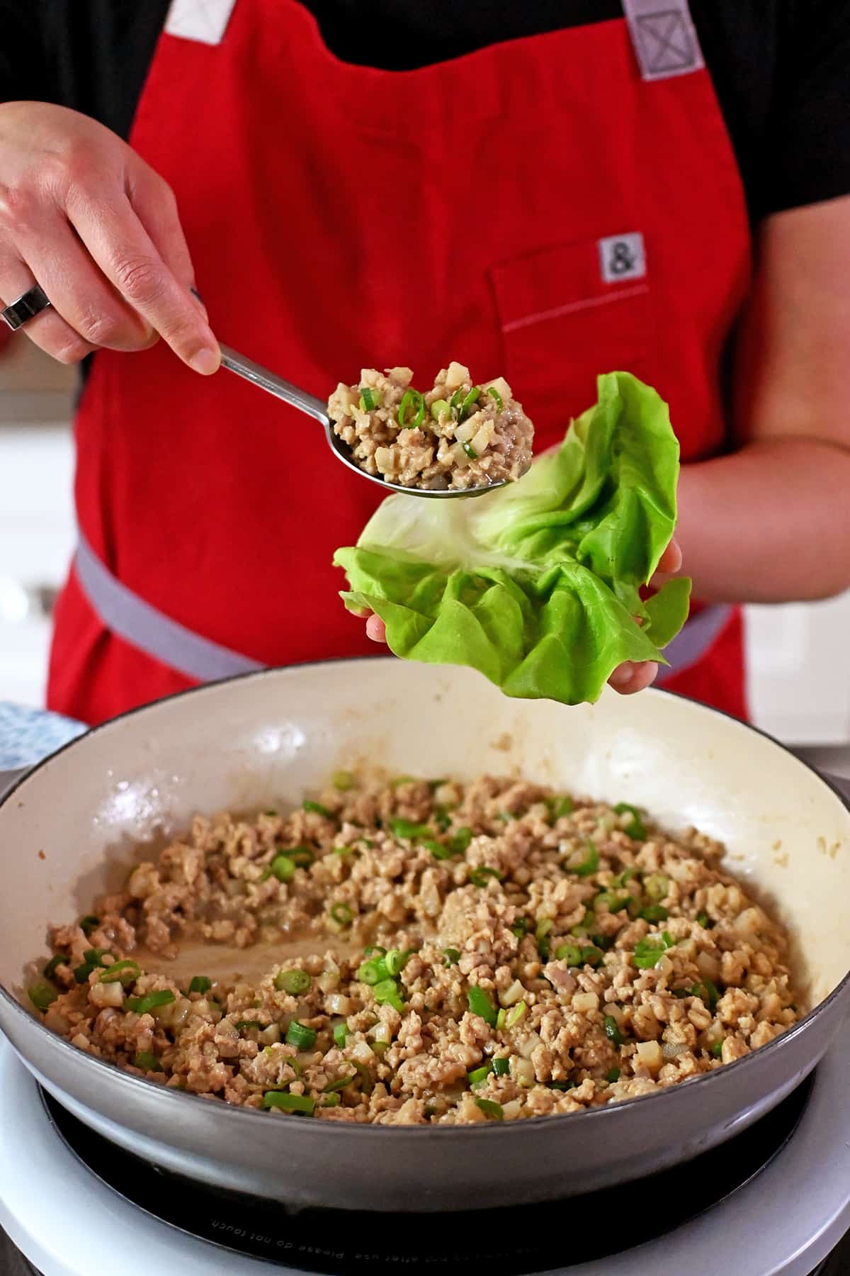 Spooning seasoned ground chicken from a skillet into a lettuce leaf.