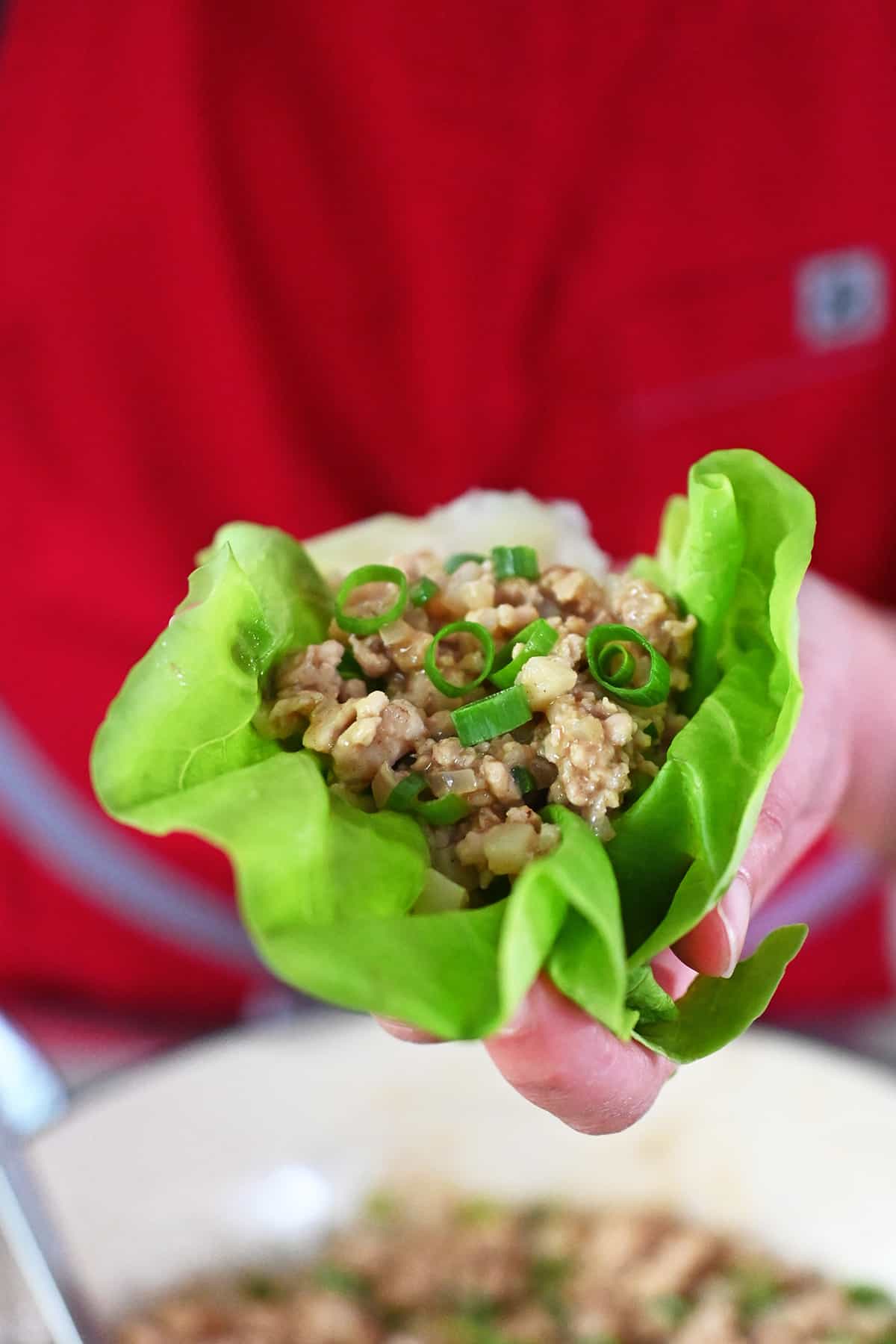 A hand holding a chicken lettuce wrap over a skillet filled with the filling.