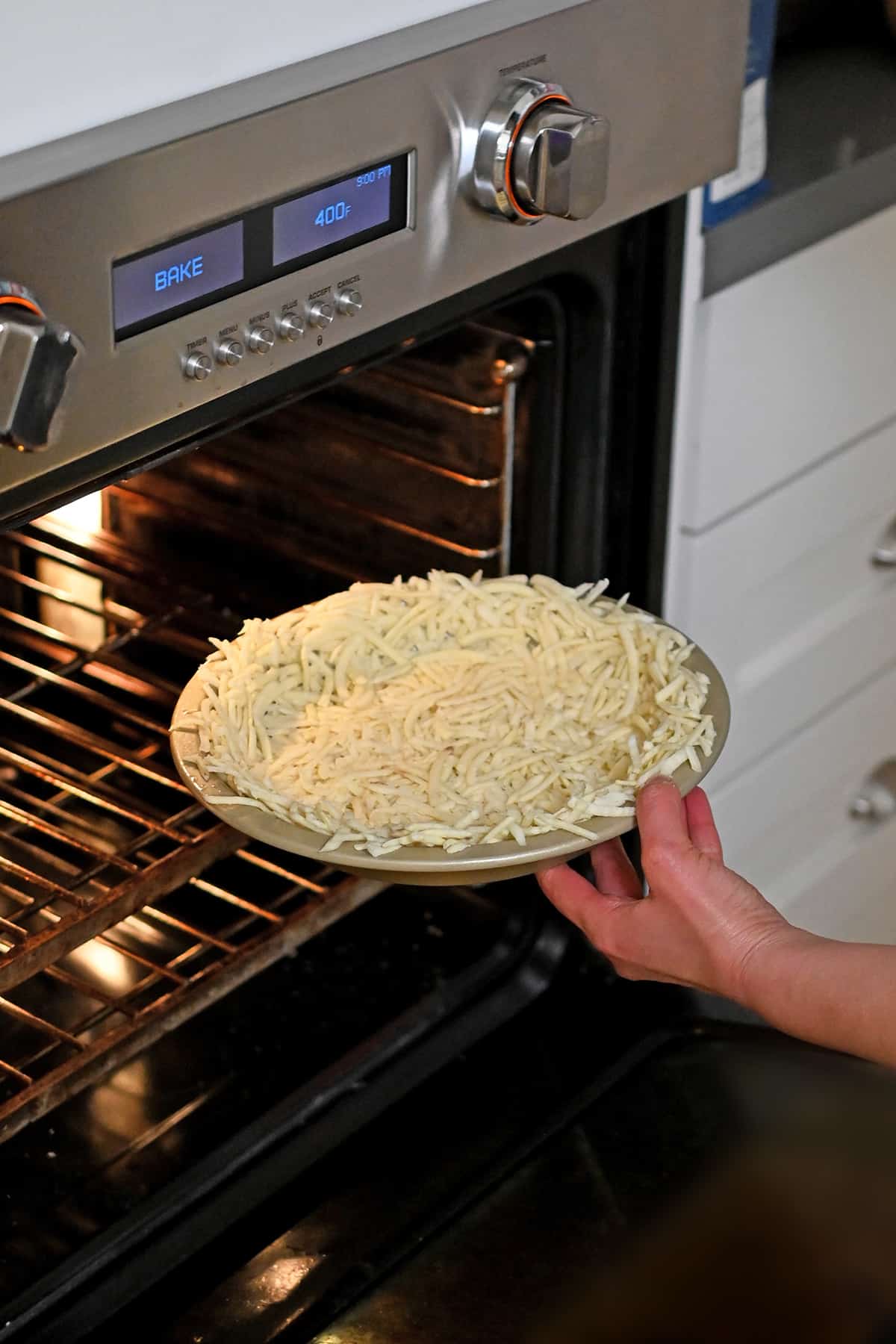 Putting a shredded potato crust lined pie plate into the oven.