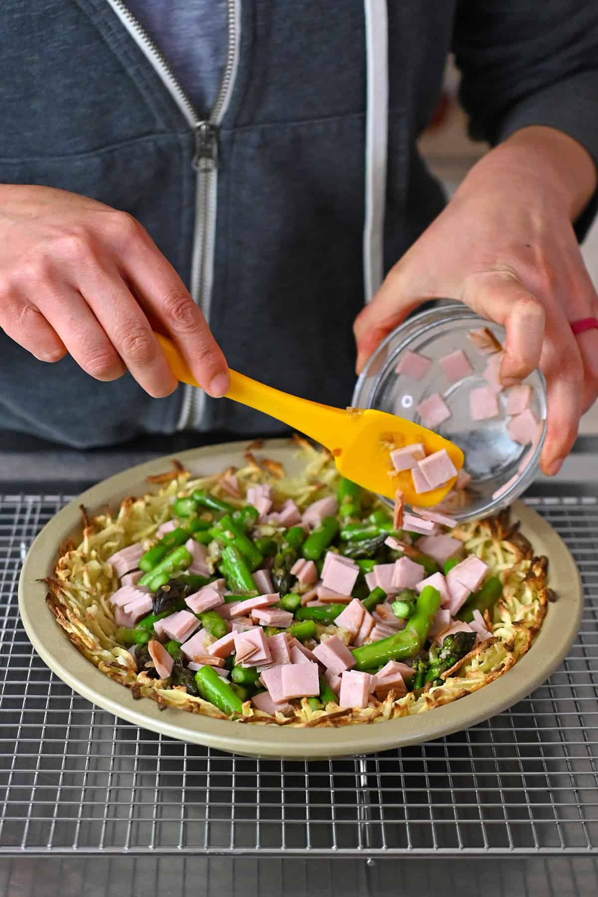 Adding cooked asparagus and diced ham to a baked shredded potato crust in a pie plate.
