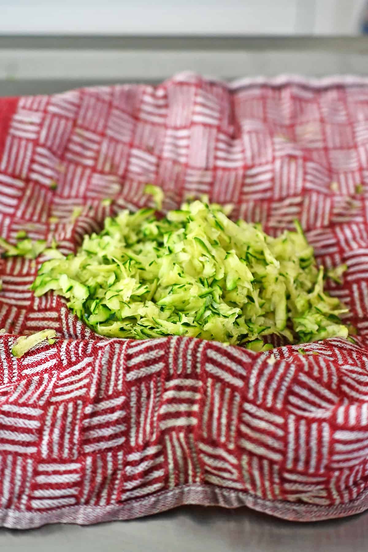 Shredded zucchini that has been squeezed dry in a red and white kitchen towel.