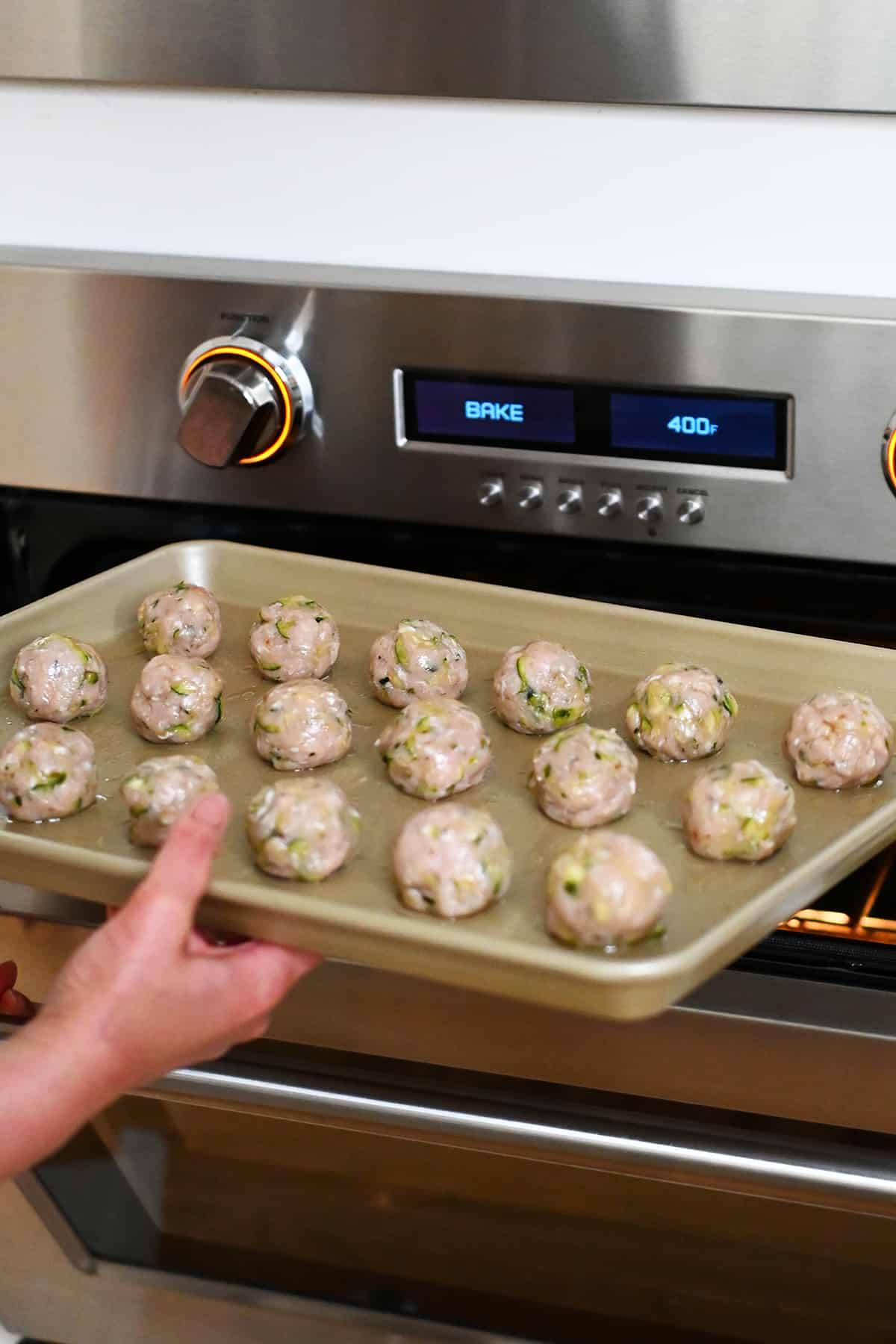 Placing a tray of chicken meatballs into a 400 F degree oven.