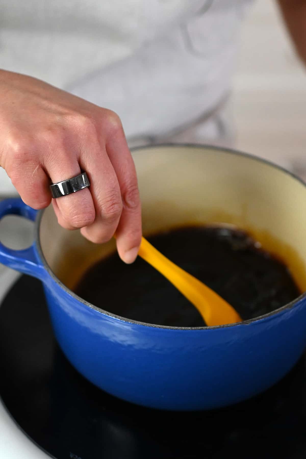 Stirring paleo and Whole30 teriyaki sauce in a small saucepan with a yellow silicone spatula.