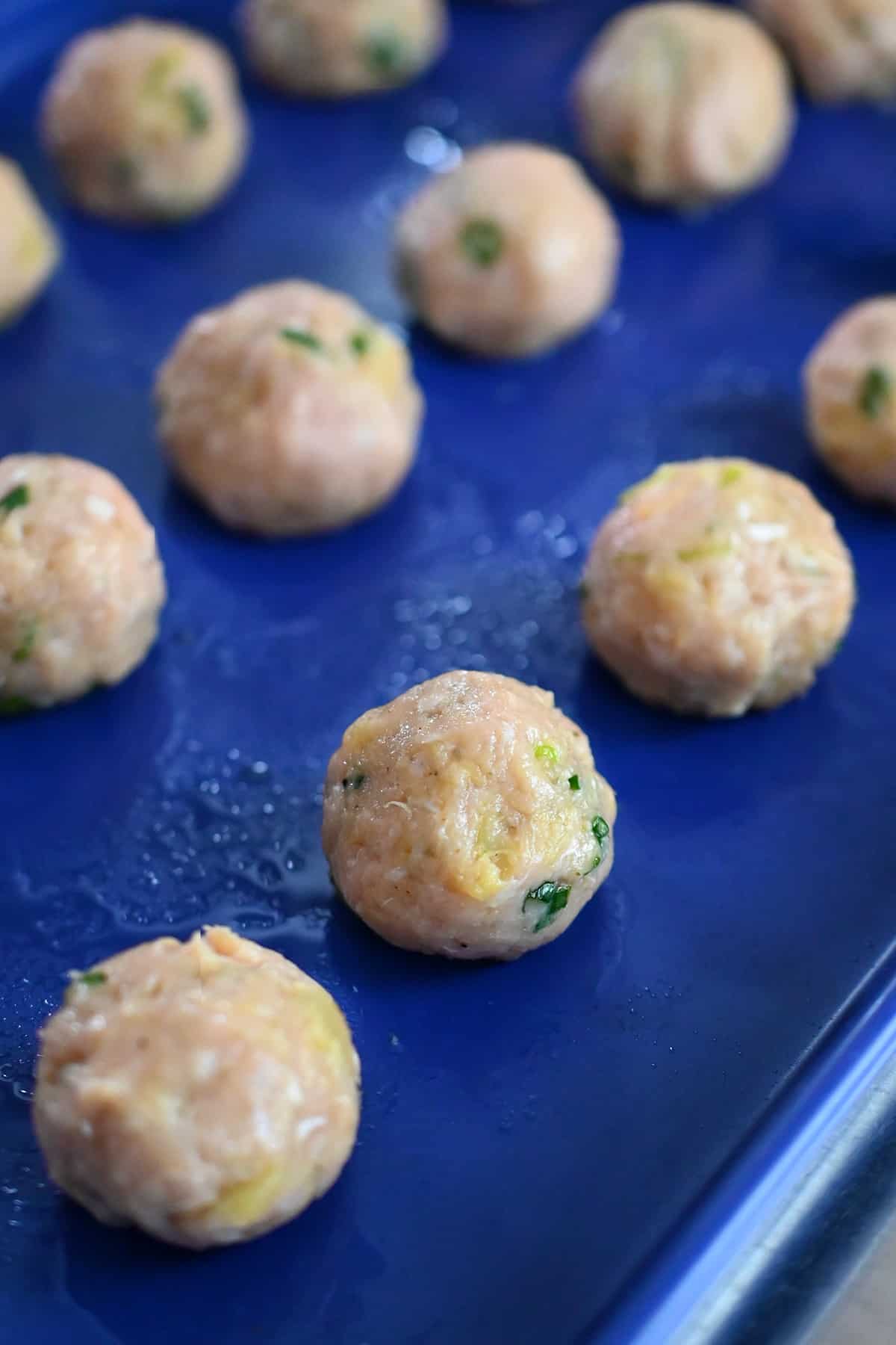 A closeup of raw teriyaki pineapple meatballs on a blue rimmed baking sheet.